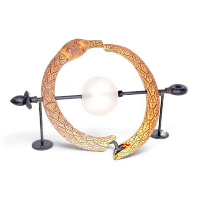 Sale Photo Thumbnail #215: Carved horn ouroboros or snake brooch featuring an incised bee head, displayed on a custom metal stand centered with a frosted glass sphere.