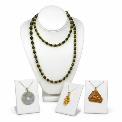 Sale Photo Thumbnail #5: Collection of fine Vintage 14k and 18K jewelry displayed on white stands, featuring a long green stone and gold bead strand necklace, a carved lavender jade pi disc pendant, a gold nugget pendant, and an amber pendant with a gold gazelle overlay.