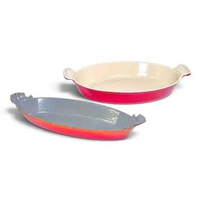 Sale Photo Thumbnail #216: Two Le Creuset enameled cast iron oval baker dishes in gradient red/orange hues with integrated side handles.
