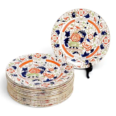 Sale Photo Thumbnail #223: Stack and display of Imari-style porcelain dinner plates featuring intricate floral motifs in orange, cobalt blue, and green hues with gilded accents.