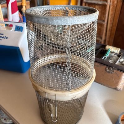 Sale Photo Thumbnail #76: Vintage wire mesh fish basket featuring a spring-loaded trap door and metal rim.