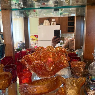 Sale Photo Thumbnail #93: Collection of vintage carnival glass tableware, including a ruffled marigold bowl, banana boat dish, and small toothpick holders displayed in a cabinet.