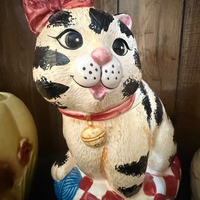 Sale Photo Thumbnail #32: Vintage painted ceramic cat cookie jar, featuring a black-and-white spotted cat with a red hair bow and bell collar sitting on a checkered cushion with a ball of blue yarn.