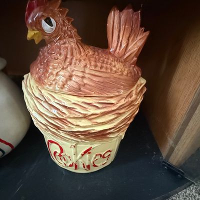 Sale Photo Thumbnail #28: Vintage ceramic rooster-on-a-nest cookie jar, featuring embossed red text on the cream-colored base with slight paint wear.