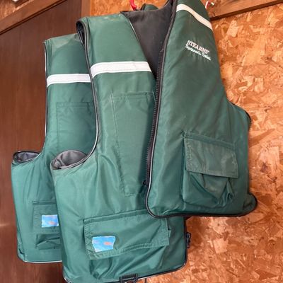 Sale Photo Thumbnail #80: Set of three green Stearns Sportsman's Series life jackets with reflective strips and front pockets hanging on wall hooks.