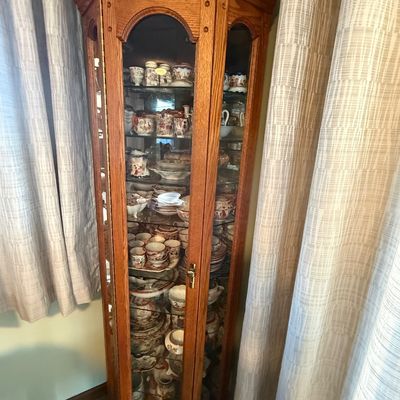 Sale Photo Thumbnail #15: Traditional oak corner display cabinet with arched glass door panels, interior lighting, and glass shelving, filled with a collection of fine china.