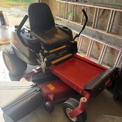 Sale Photo Thumbnail #85:  zero-turn riding lawn mower stored in a garage, featuring a black high-back seat and a red cutting deck. 50”deck.