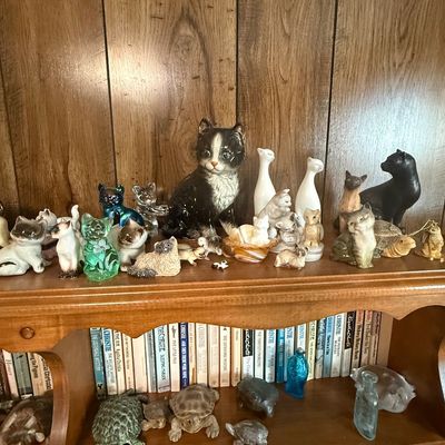 Sale Photo Thumbnail #37: A collection of vintage cat figurines displayed on a wooden bookshelf, alongside a lower shelf of turtle figurines and Agatha Christie paperbacks.