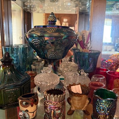 Sale Photo Thumbnail #92: Collection of vintage glass tableware displayed in a cabinet, including a blue carnival glass covered candy dish with grape motif and small decorative toothpick holders.