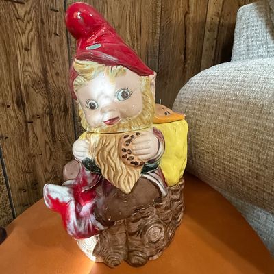 Sale Photo Thumbnail #23: Vintage hand-painted ceramic gnome cookie jar featuring a gnome holding a chocolate chip cookie and seated on a tree stump, showing minor paint wear.