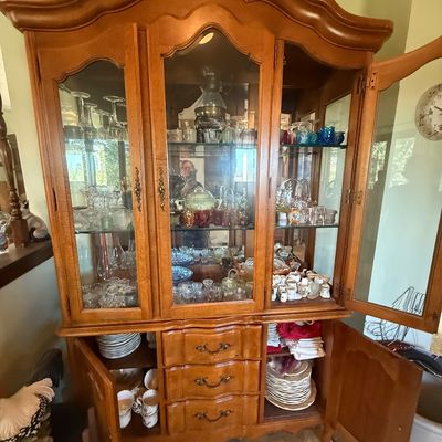 Sale Photo Thumbnail #18: French Provincial style wooden china hutch featuring glass display doors, three central drawers, lower cabinet storage, and an assortment of glassware and china.