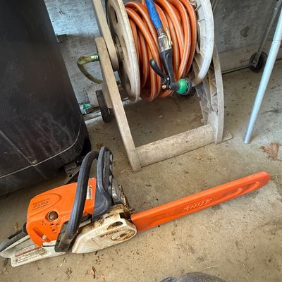 Sale Photo Thumbnail #71: Stihl gas-powered chainsaw with an orange bar scabbard, shown next to a mobile hose reel cart.