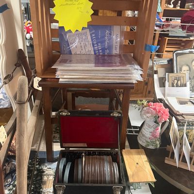Vintage black carrying case filled with film reels, sitting in front of a wooden display crate with sheet music and collectible...