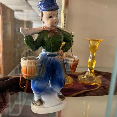 Vintage ceramic figurine of a boy carrying water buckets, displayed alongside an amber glass candlestick holder.