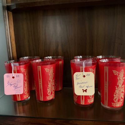 Set of vintage red and gold Thai princess drinking glasses displayed on a shelf.