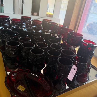 Large collection of vintage ruby red pressed glass goblets and a matching divided candy dish displayed on a mirrored tray.