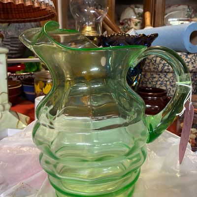 Vintage green uranium glass pitcher with a ribbed, beehive design and ice lip, displayed on a table.