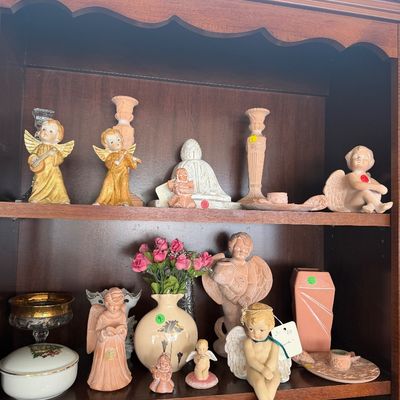 A wooden display hutch filled with an assortment of vintage angel figurines, terracotta decor, ceramic vases, and glassware.
