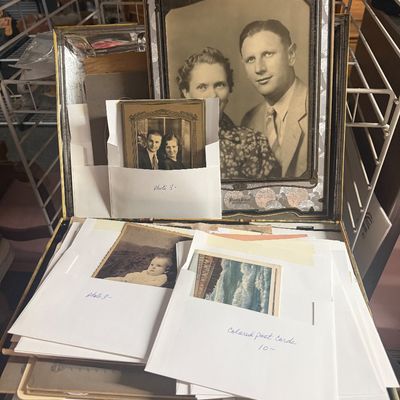 Vintage photo album box filled with framed black-and-white family portraits, postcards, and old photographs, dating from the early to...