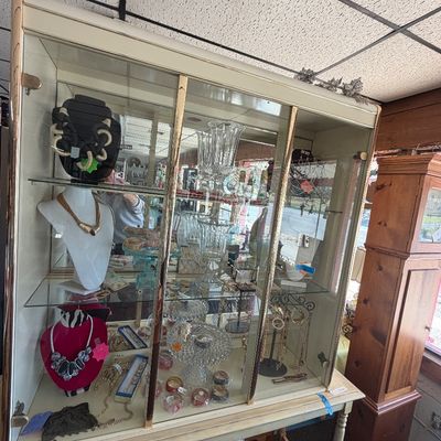 Vintage glass display cabinet filled with costume jewelry, crystal vases, and decorative glassware.