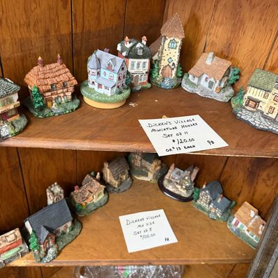 Collection of Dickens' Village miniature resin collectible houses displayed across two wooden shelves.