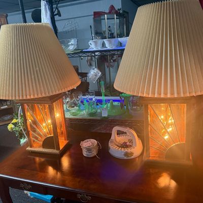 Pair of vintage illuminated wooden table lamps with sunburst brass details and pleated cream shades, displayed alongside a ceramic dish...