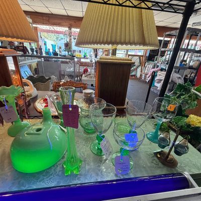 Collection of vintage green glassware, including glowing uranium glass pieces displayed under blacklight, alongside table lamps with...