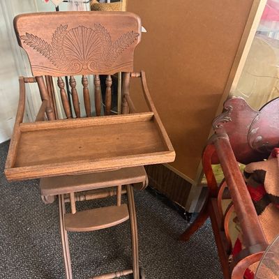 Vintage convertible wooden high chair with a carved shell crest, turned spindles, attached tray, and wheels.