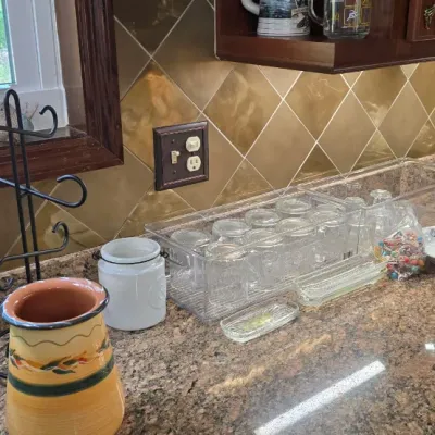 Sale Photo Thumbnail #12: Kitchen counter assortment including clear plastic organizer bins with glassware, a pottery vase, punch bowl, and a black wrought-iron mug tree.