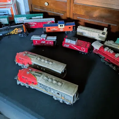 Sale Photo Thumbnail #93: Collection of Lionel and assorted model train cars and engines, including Santa Fe locomotives, festive holiday cars, and a Harley-Davidson tanker car.