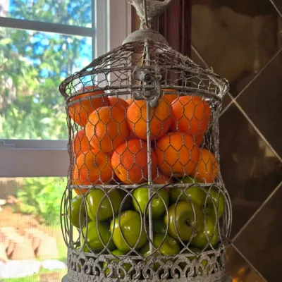 Sale Photo Thumbnail #10: Rustic whitewashed wire birdcage hanging fruit basket filled with artificial oranges and green apples.