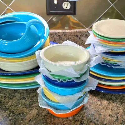 Sale Photo Thumbnail #17: Collection of colorful Fiestaware ceramic dinnerware, including stacks of plates, bowls, and a gravy boat in turquoise, cobalt blue, green, yellow, and ivory.