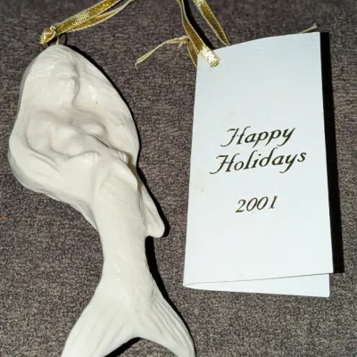 Sale Photo Thumbnail #51: White porcelain mermaid holiday ornament with gold hanging ribbon, accompanied by a tag printed "Happy Holidays 2001".