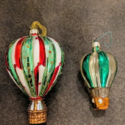 Sale Photo Thumbnail #76: Two glass hot air balloon Christmas ornaments, featuring a large glitter-embellished red, green, and white ornament alongside a smaller vintage green and gold striped balloon.