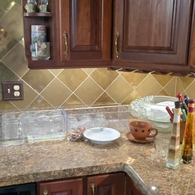Sale Photo Thumbnail #8: Assorted kitchenware and decor including decorative glass oil bottles, clear glass mugs in acrylic holders, ceramic pottery, and glass punch bowls arranged on a granite countertop.