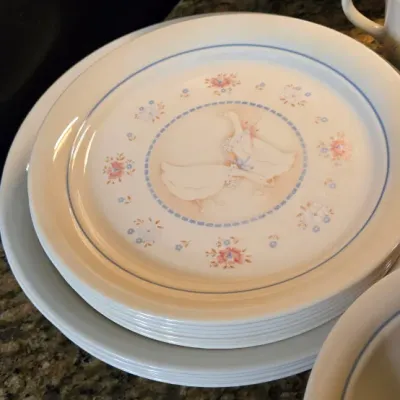 Sale Photo Thumbnail #20: Stack of vintage country-style ceramic dinner plates featuring a central goose design and blue floral border, alongside a matching pitcher.