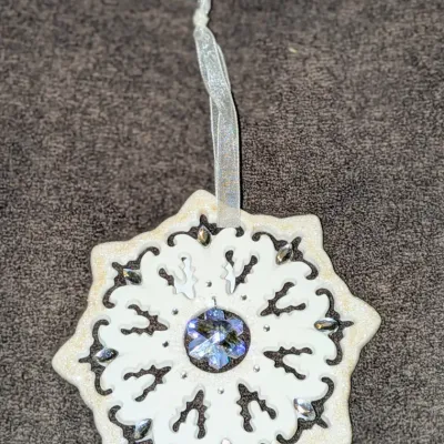Sale Photo Thumbnail #50: Intricate white snowflake Christmas ornament featuring iridescent crystal embellishments, glittered accents, and a sheer hanging ribbon.
