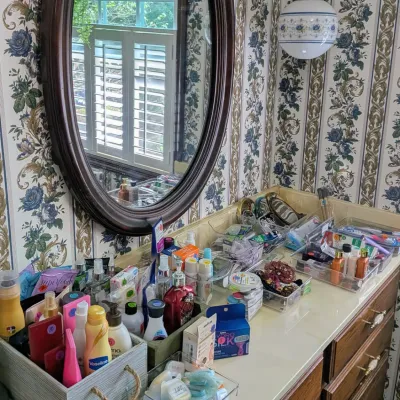 Sale Photo Thumbnail #89: Bathroom vanity counter organized with various personal care products, toiletries, and clear storage bins, set below a large oval wooden framed mirror.