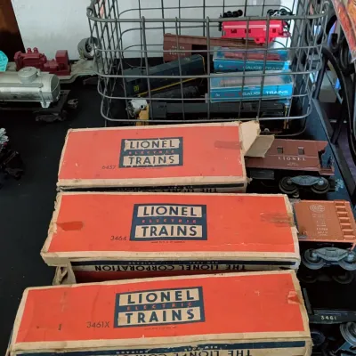Sale Photo Thumbnail #92: Vintage Lionel model train cars in original orange and blue boxes alongside loose train cars and a metal wire basket.