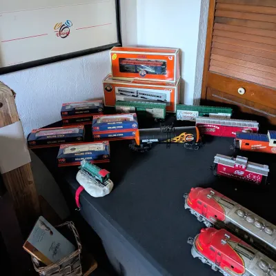 Sale Photo Thumbnail #94: Collection of vintage model train cars and locomotives, including boxed Lionel HO scale rolling stock, Harley-Davidson tanker car, and holiday-themed cars.