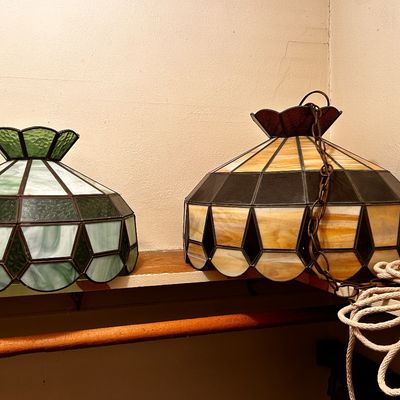Sale Photo Thumbnail #113: Two vintage Tiffany-style leaded slag glass lamp shades, featuring green and amber-hued geometric panel designs.