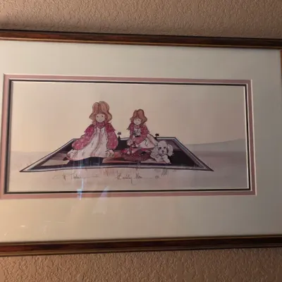 Framed and signed artwork depicting two young girls and a dog on a rug, double-matted in a dark wooden frame.