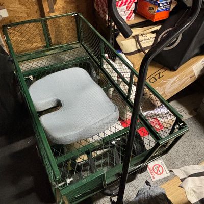 Green metal utility garden cart with fold-down mesh sides and a long padded handle,