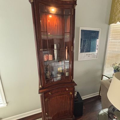 Traditional mahogany corner hutch with interior lighting, leaded glass doors, and inlaid wood detailing.