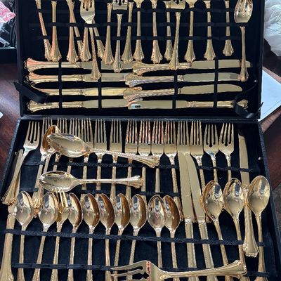 Large gold-plated flatware set with ornate scroll handles, neatly arranged in a black velvet-lined storage case.