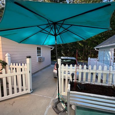 Large turquoise outdoor patio umbrella with a black metal frame, set outdoors near a garden bed and fence.