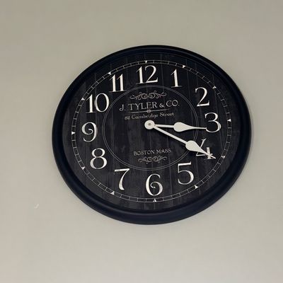 Round vintage-style wall clock featuring a black faux-wood-plank face, white numerals, and 'J. Tyler & Co. Boston Mass.' text.