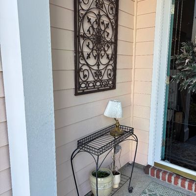 Black wrought iron rectangular plant stand console table alongside a wall-mounted wrought iron scrollwork wall art panel.