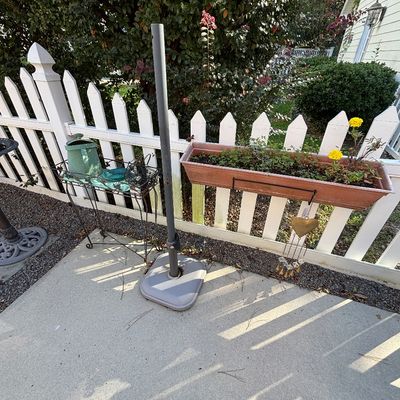 Outdoor patio items featuring a plastic window box planter with yellow marigolds, a metal patio umbrella stand, and a wrought iron plant...