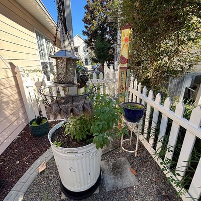Rustic outdoor garden decor collection including a painted metal trash can planter, a hanging solar lantern with wire basket, and a...